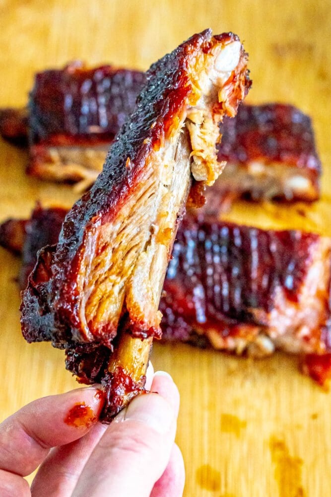 A person holding smoked pork ribs on a cutting board.
