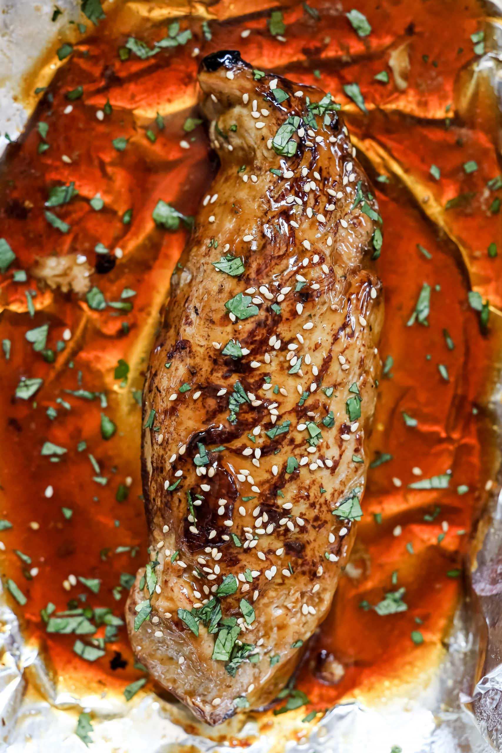 A piece of chicken in foil with teriyaki sauce on it.