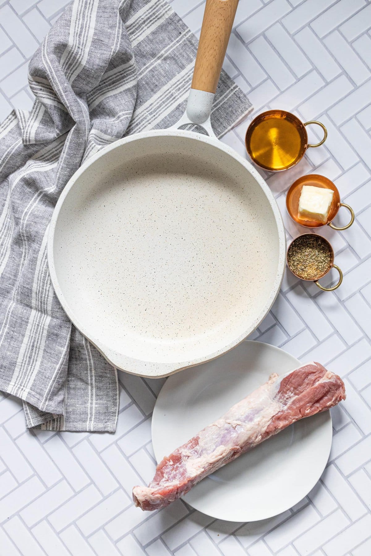 pork, olive oil, herbs, and a pan on a table