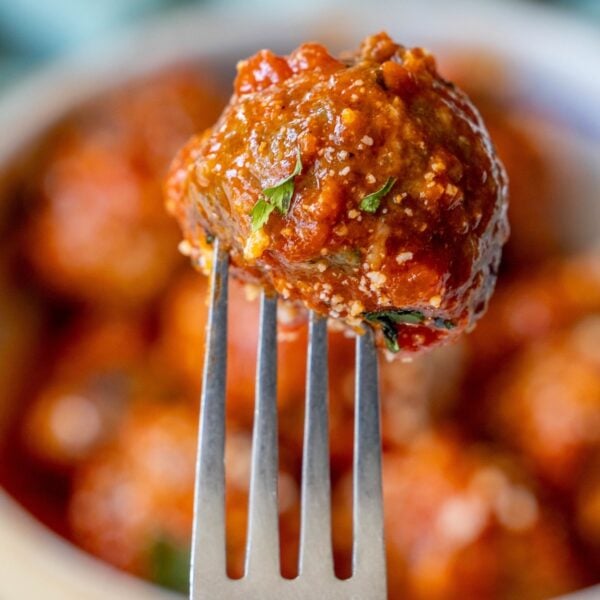 A meatball covered in tomato sauce and garnished with parsley is held on a fork against a background of other meatballs, showcasing the best easy meatballs.