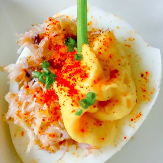 A deviled egg topped with mustard, chives, and inspired by a Bloody Mary.