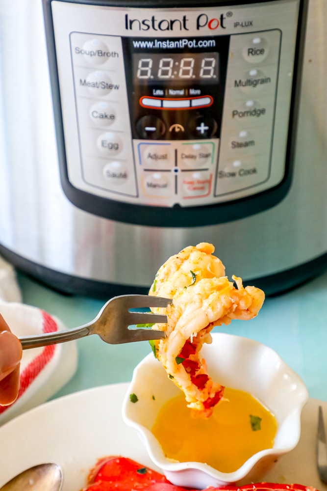 A person is holding a fork in front of an instant pot cooking lobster tails.