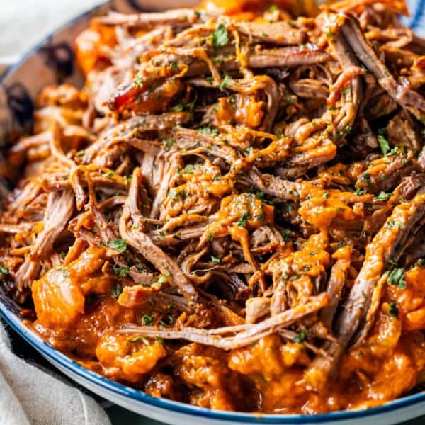 Shredded beef in a rich, orange-red tomato soup pot roast sauce garnished with chopped herbs, served in a shallow bowl.