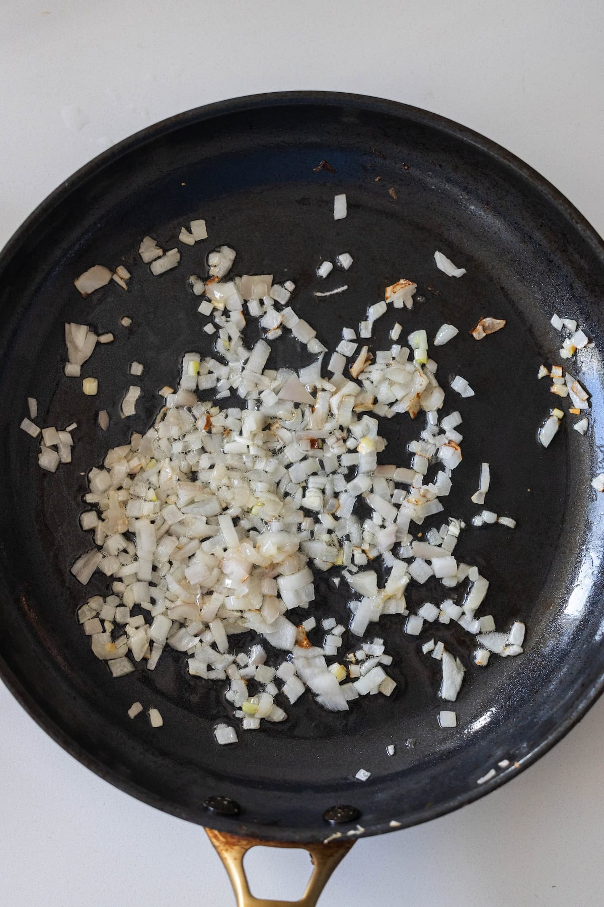 Chopped onions being saut&eacute;ed in a black frying pan on a white surface, perfect as a savory base for Tuscan roasted white beans.