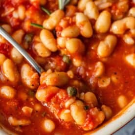 Close-up of Tuscan roasted white beans in a tomato-based sauce with herbs, served in a bowl with a spoon.