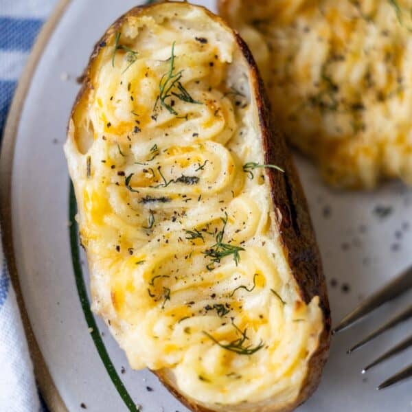 A delicious Twice Baked Potato half filled with creamy mashed potatoes, garnished with herbs and black pepper, served on a plate with a fork nearby.
