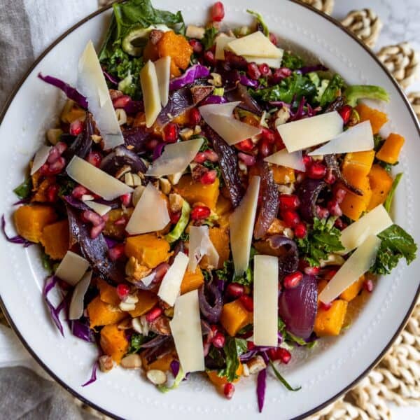 A plate of winter salad with kale, roasted butternut squash, red onions, purple cabbage, pomegranate seeds, walnuts, and shaved cheese.