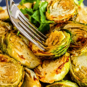 A fork piercing roasted Brussels sprouts garnished with parsley, these air-fried delights are part of a keto-friendly recipe that elevates your meal with crisp texture and vibrant flavors.