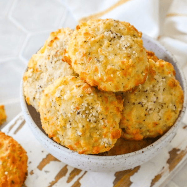 A bowl of freshly baked keto garlic cheese muffins sprinkled with herbs on a white wooden background.