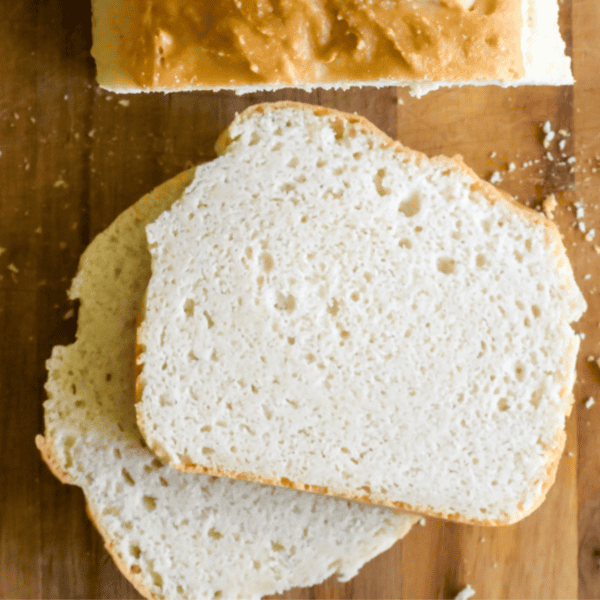 A loaf of homemade keto bread with two slices cut on a wooden surface. The bread has a light, airy texture and a golden-brown crust, perfect for your favorite easy keto sandwich recipe.