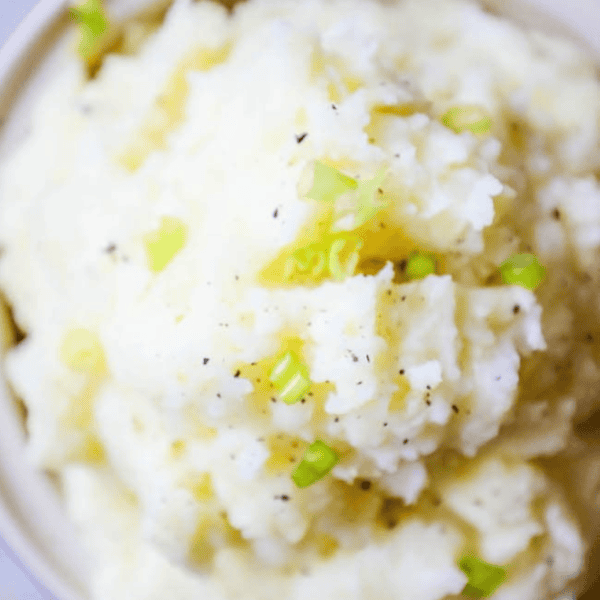 A bowl of slow cooker mashed potatoes topped with chopped green onions and black pepper.